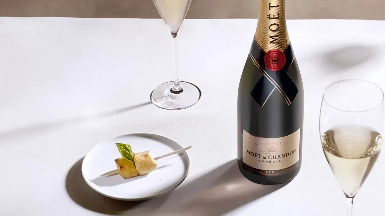 Moët & Chandon Champagnerflasche neben einem Glas Champagner und einem kleinen Häppchen. Das Etikett zeigt das Gründungsjahr, was auf den Degorgierdatum Champagner hinweist.