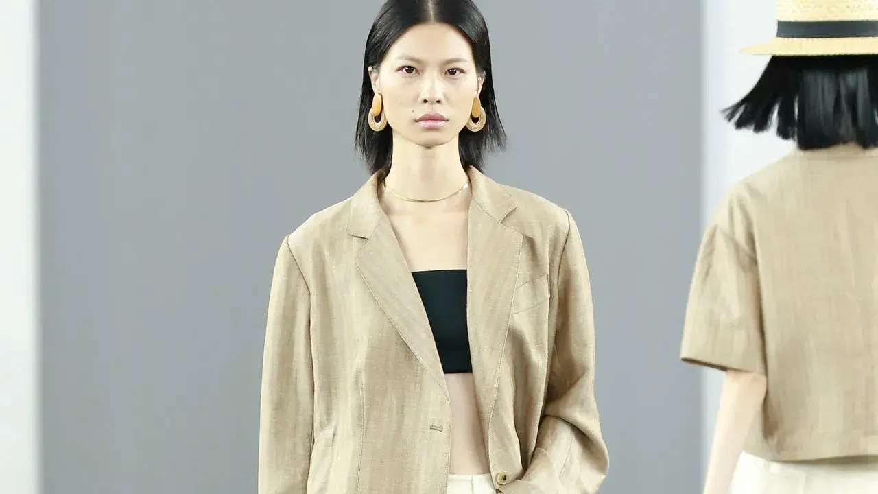 Ein Model trägt einen beigen Blazer aus knitterndem Leinen mit einem schwarzen Top. Große, runde Ohrringe schmücken ihre Ohren.