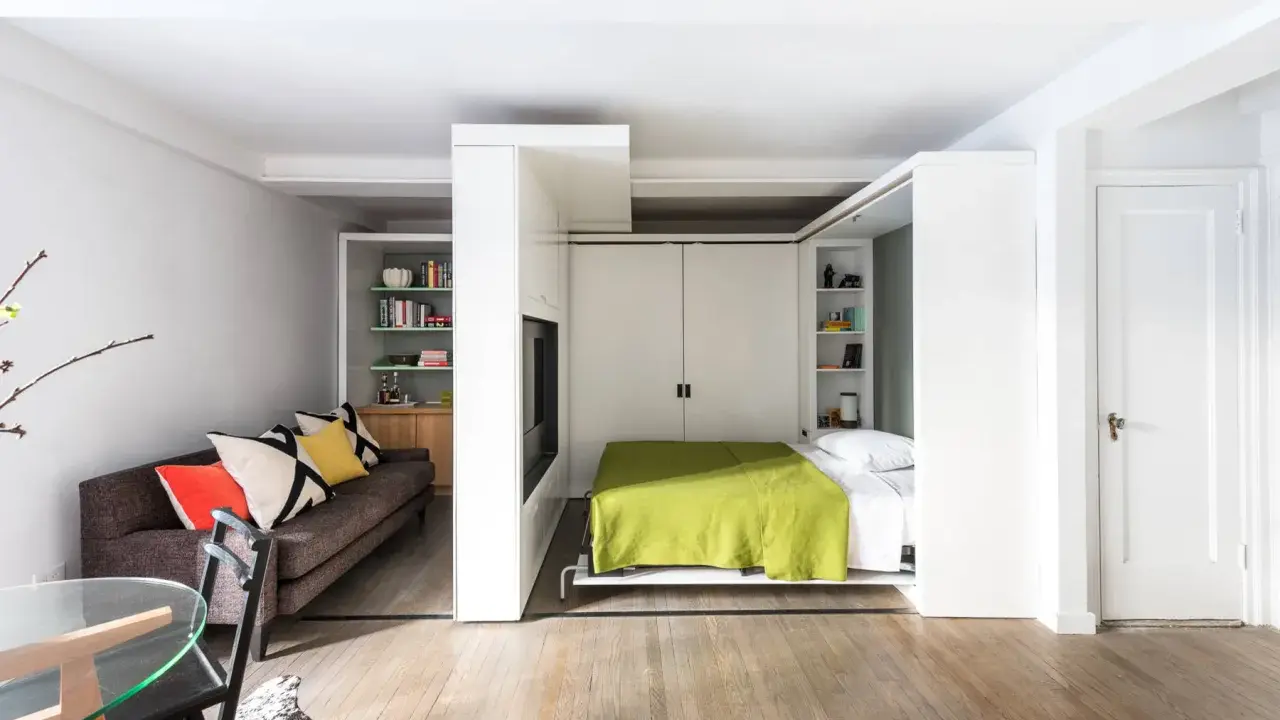 En modern lägenhet med smarta lösningar. En bekväm soffa i vardagsrumsdelen och en inbäddad säng med grön filt i sovrummet.