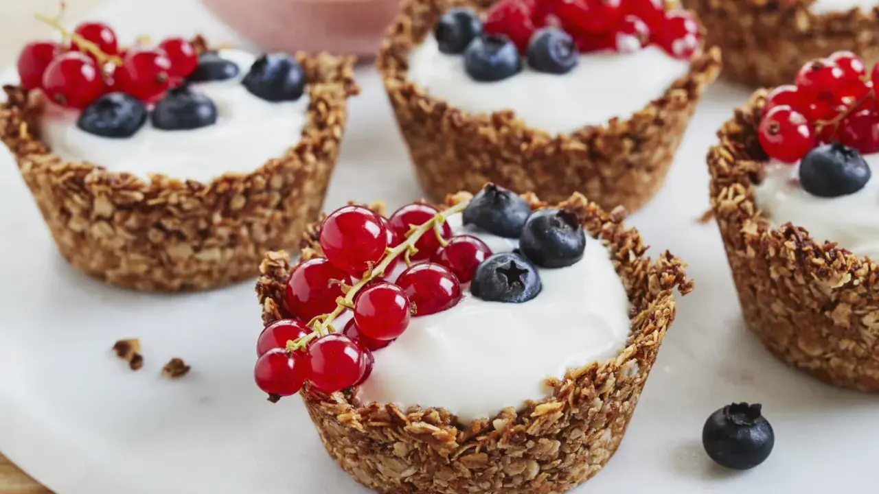 Leckere Granola Cups gefüllt mit Joghurt und garniert mit roten Johannisbeeren und Blaubeeren.