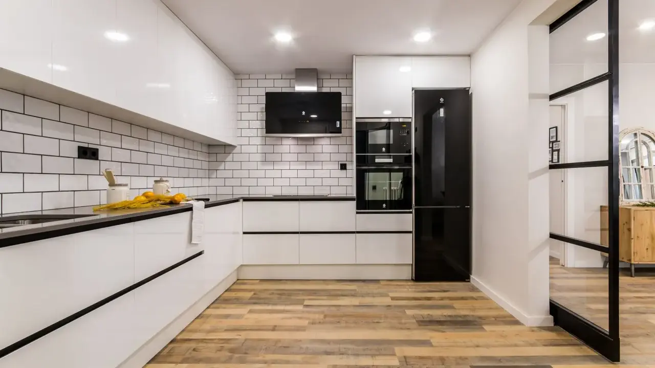 Cocina moderna con pared cocinas mitad azulejo mitad pintura blanca, electrodomésticos negros y suelo de madera.