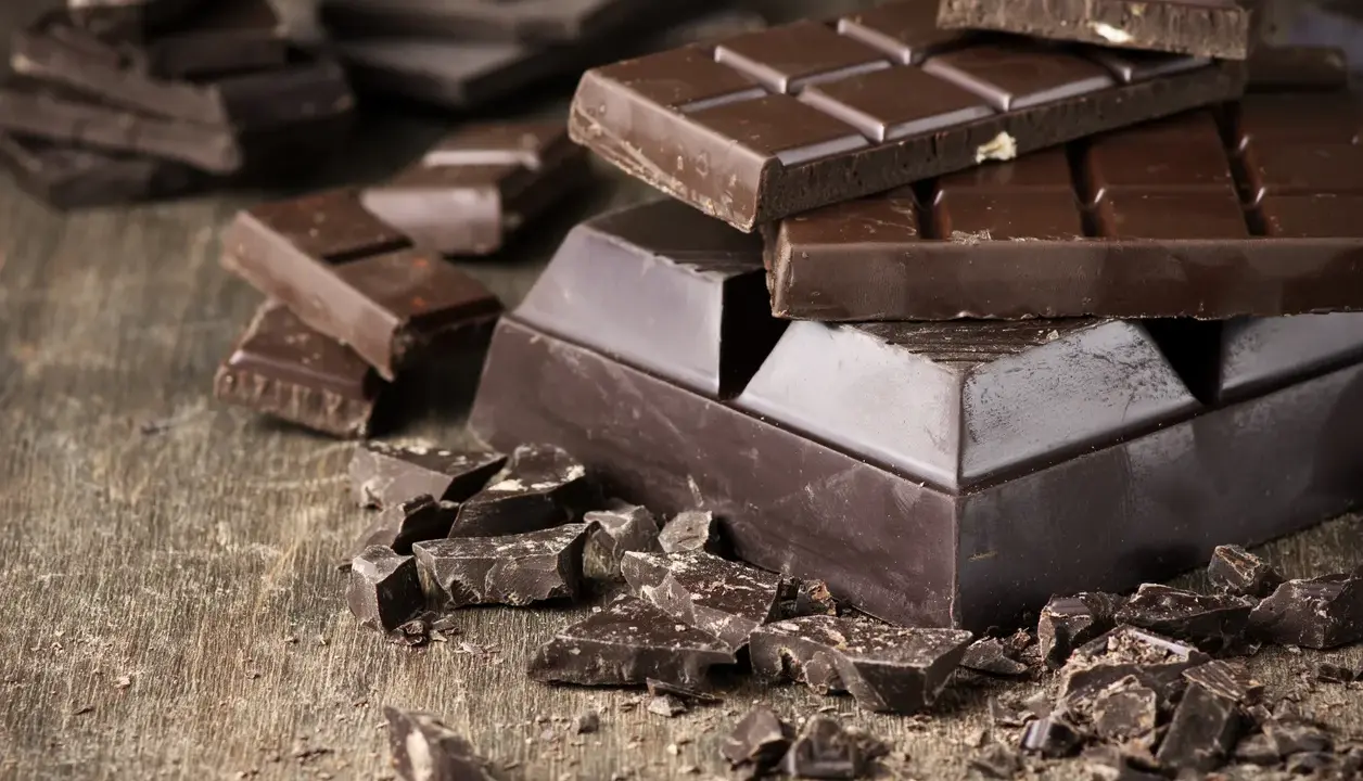 Des morceaux de chocolat noir, entiers et brisés, sur une table en bois. Une invitation à découvrir comment adoucir le chocolat noir pour une dégustation parfaite.