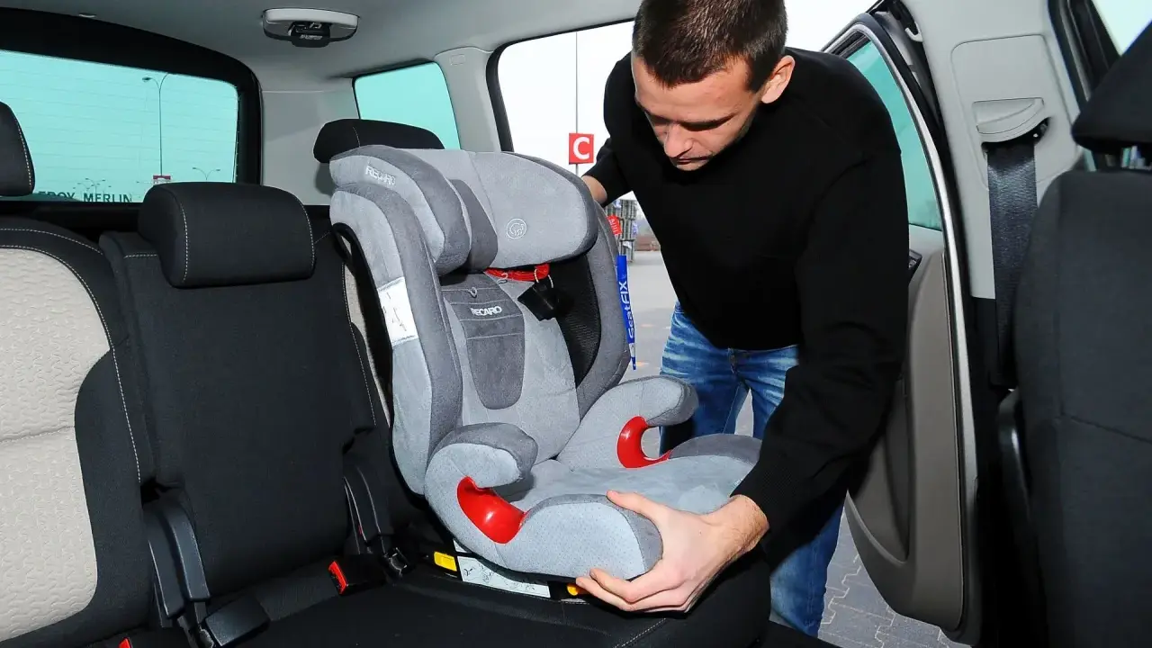 Mężczyzna montuje fotelik dziecięcy, pokazując, jak zamontować isofix w aucie.