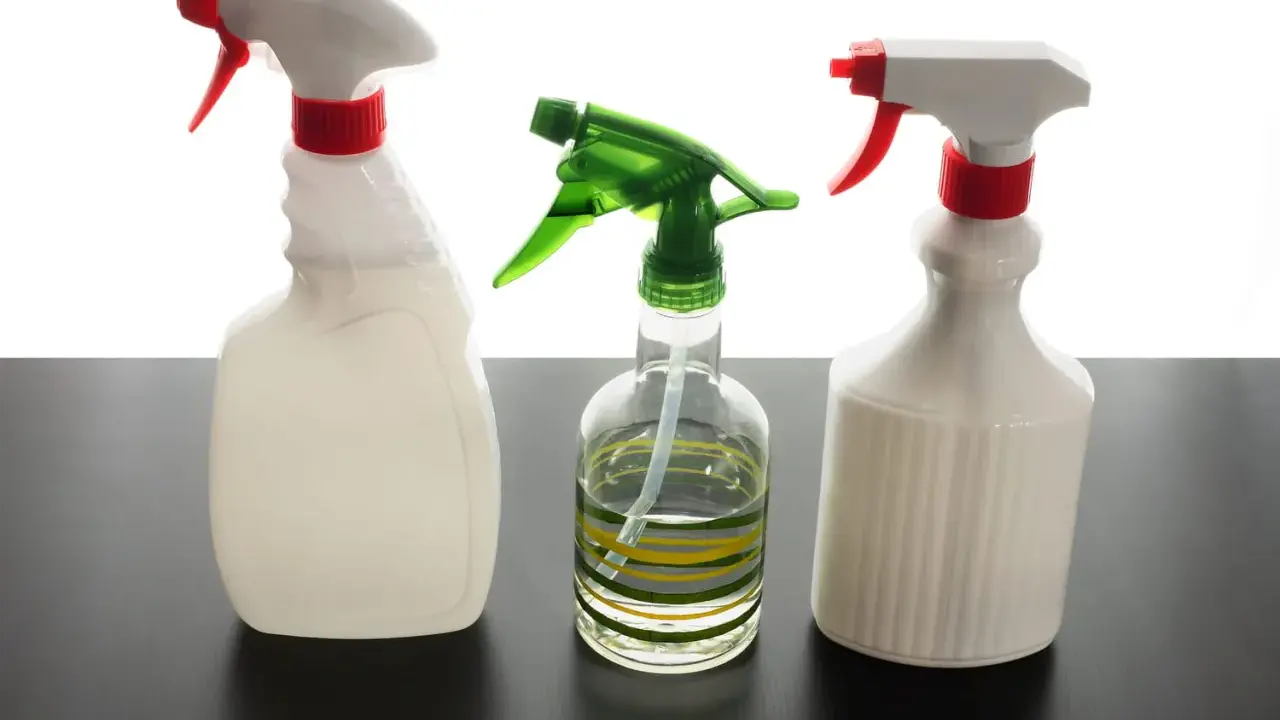 Trois flacons pulvérisateurs, dont un transparent avec des rayures vertes et jaunes, suggèrent un désinfectant naturel pour un nettoyage écologique.