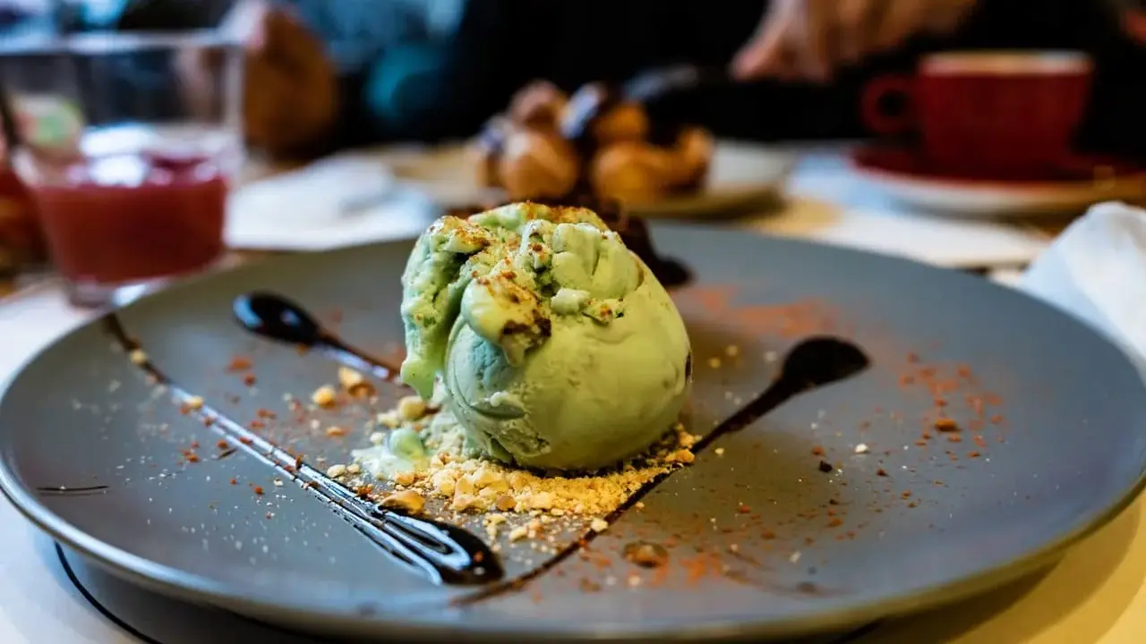 Pyszne lody pistacjowe na talerzu, ozdobione czekoladą i posypką. Idealny deser na poprawę humoru.