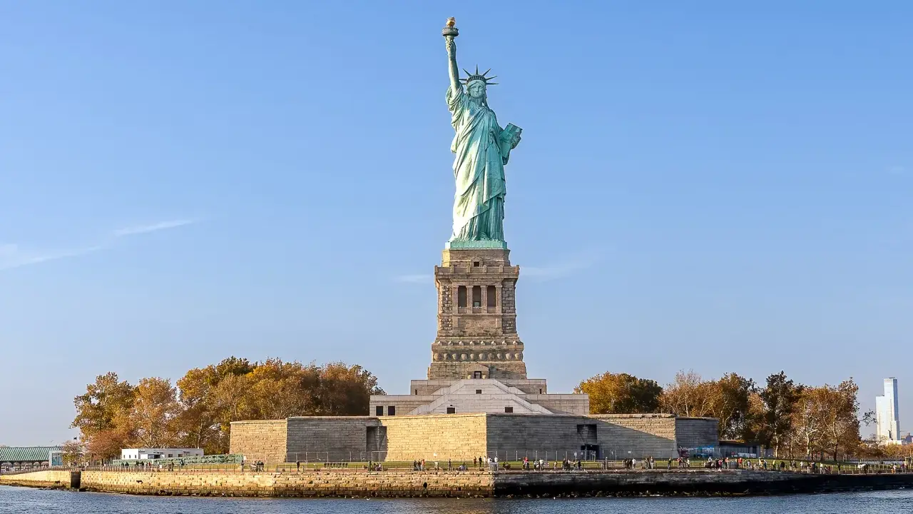 Gdzie jest Statua Wolności? Na Liberty Island, w Nowym Jorku, wznosi się dumnie symbol wolności, otoczona jesiennymi drzewami i błękitnym niebem.