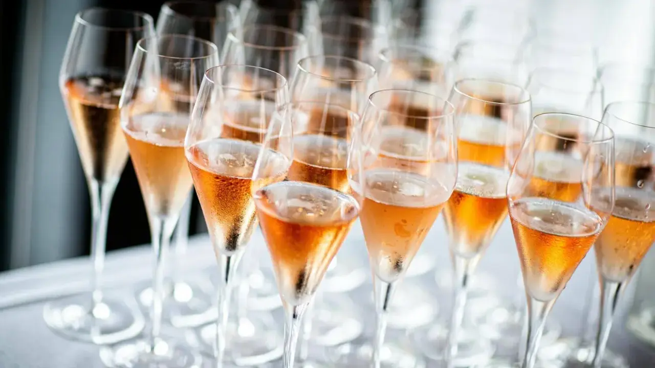 Reihe von Champagnergläsern mit Rosé-Champagner, bereit für den Genuss. So trinkt man Champagner: mit Stil und Freude.