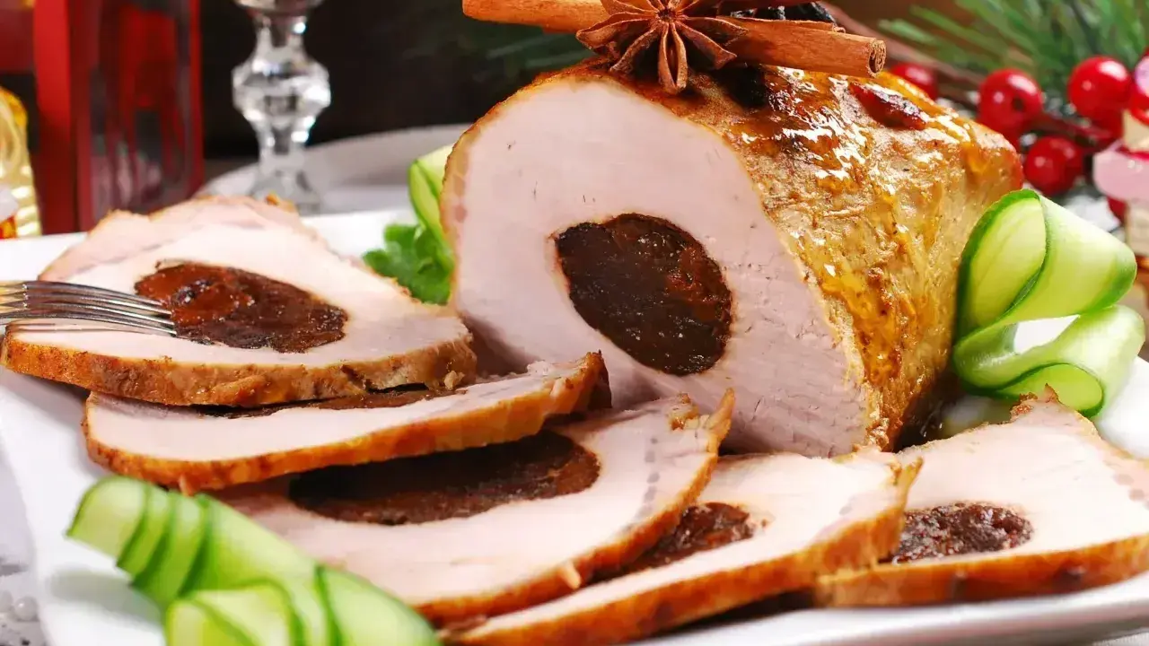 Pyszny schab ze śliwką, pieczony z przyprawami, podany z ogórkiem i dekoracjami świątecznymi.