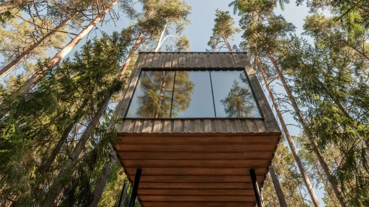 Ett modernt **wood hotel** i en svensk skog, med stora fönster som speglar träden.