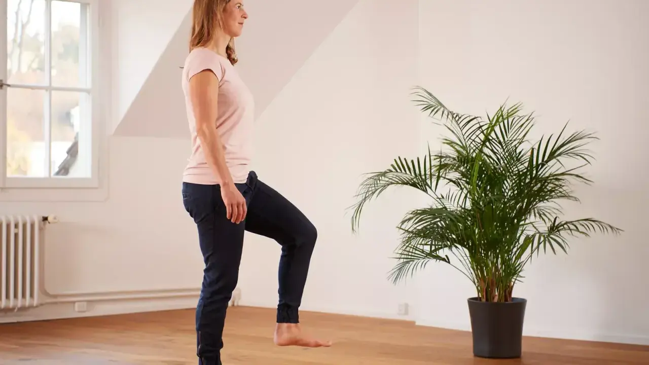 Frau übt auf einem Bein stehen im hellen Raum, neben einer grünen Palme.