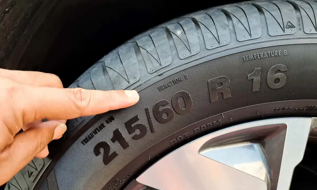Palec wskazuje na oponę, gdzie widoczny jest rozmiar 215/60 R16. To ważny element, który określa m.in. indeks prędkości opon.