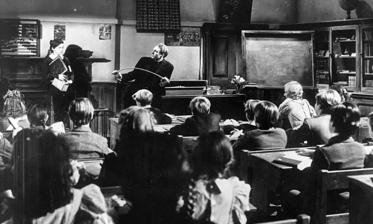 Lehrer mit Stock ermahnt Schüler in einer Klasse, die an eine Schule im Mittelalter erinnert.