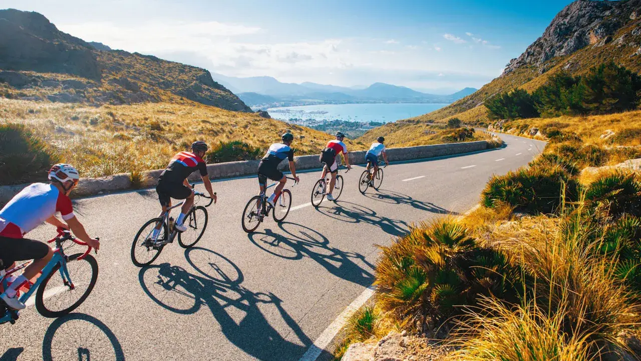 Ciclisti su una strada panoramica, esplorando i più bei percorsi in bicicletta in Italia, con il mare e le montagne sullo sfondo.