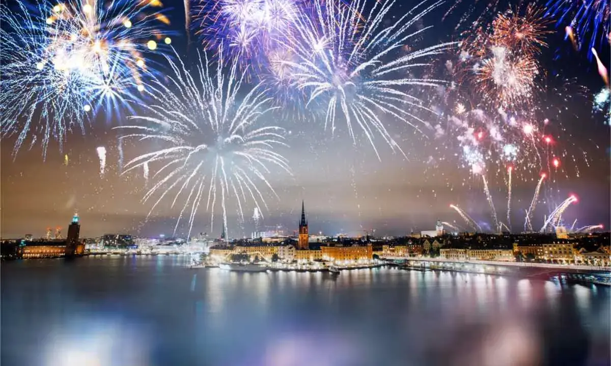 Fyrverkerier lyser upp himlen över Stockholm vid nyår. Vatten reflekterar ljusen från staden och fyrverkerierna.