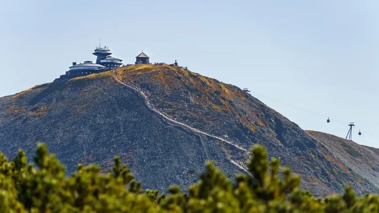 Szczyt Śnieżki w Karkonoszach, z obserwatorium i schroniskiem, po którym wije się ścieżka turystów. W tle kolejka linowa.