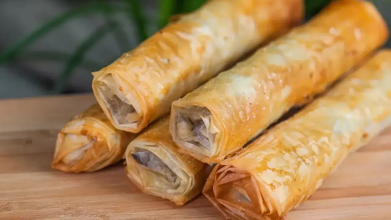 Chrupiące rolki z ciasta na baklawę, wypełnione aromatycznym farszem, ułożone na drewnianej desce.