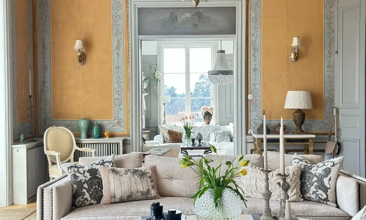 Ett elegant vardagsrum med fransk inredningsstil. Gyllene väggar, kristallkrona och antika möbler skapar en lyxig atmosfär.