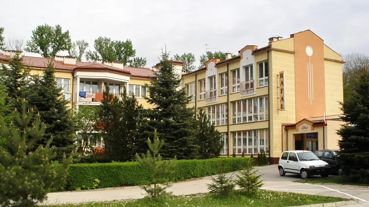 Sanatorium Rafał Busko Zdrój, z żółtą fasadą i zielenią wokół, zaprasza na wypoczynek.