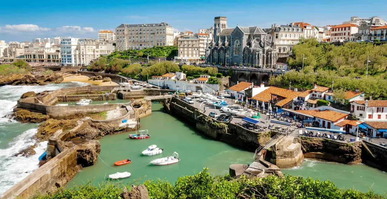 En vacker vy över hamnen i Biarritz med båtar i vattnet och en kyrka i bakgrunden. Kanske är det här tåg till Biarritz tar dig.