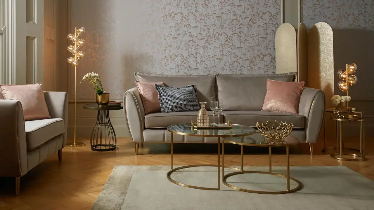 Przytulny salon glamour z beżową kanapą, różowymi poduszkami i złotymi dodatkami.