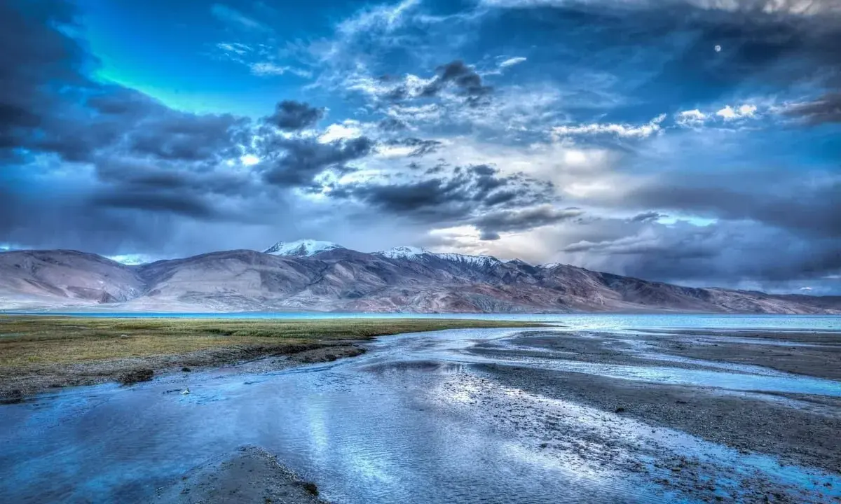 Paesaggio montano con lago e fiume, cielo drammatico con nuvole scure e luna, effetto HDR.