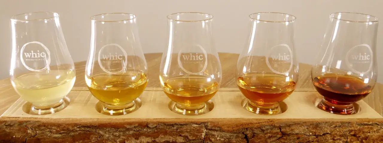Fünf Gläser mit unterschiedlichen Farben von **whiskey ohne farbstoff** stehen auf einem Holzbrett.