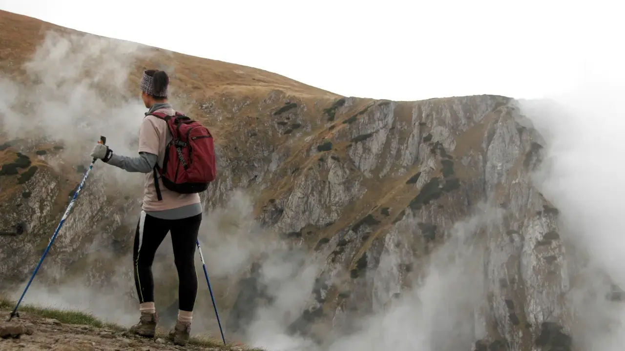 Person med ryggsäck och stavar, övar stavgång teknik på en bergssluttning med dimma.