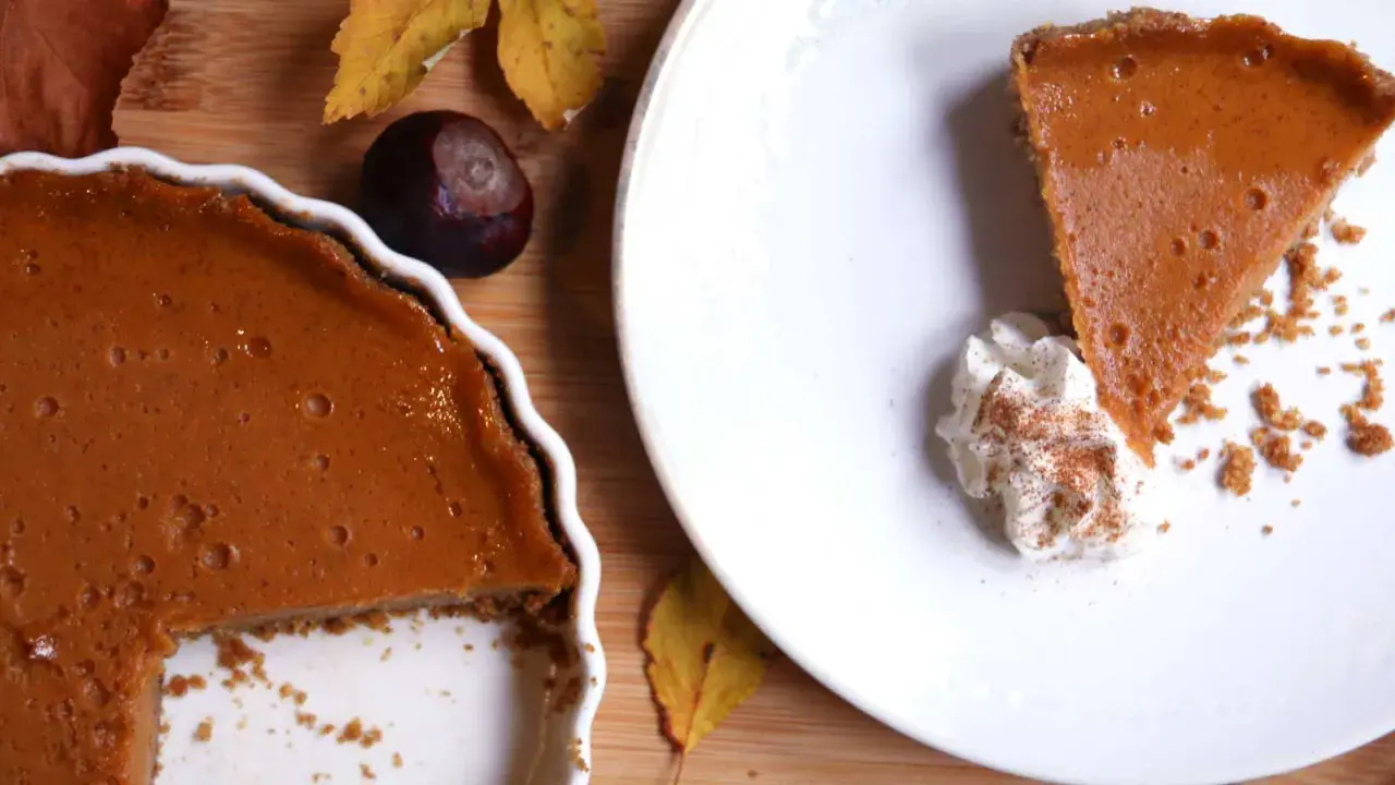 La tarta de calabaza de la abuela, con su relleno cremoso y corteza dorada, lista para ser disfrutada. Una rebanada servida con nata montada y canela.