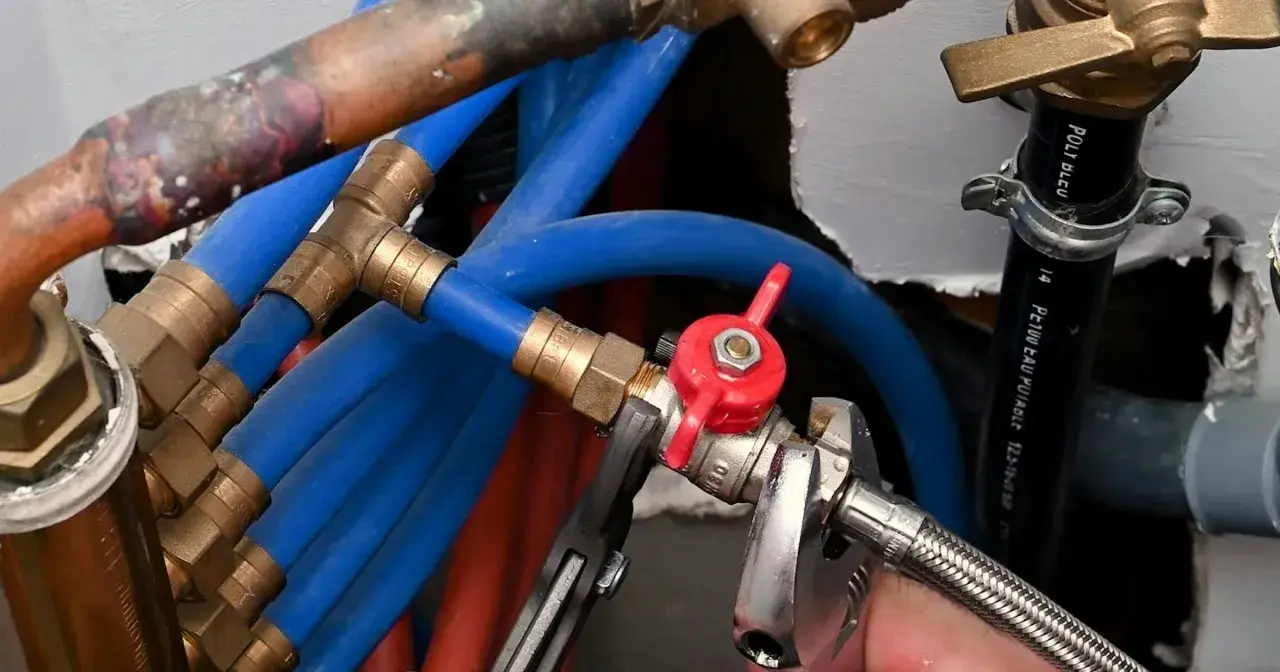 Réglage de la vanne arrivée d'eau maison avec une clé. Tuyaux bleus et rouges, raccords en laiton.