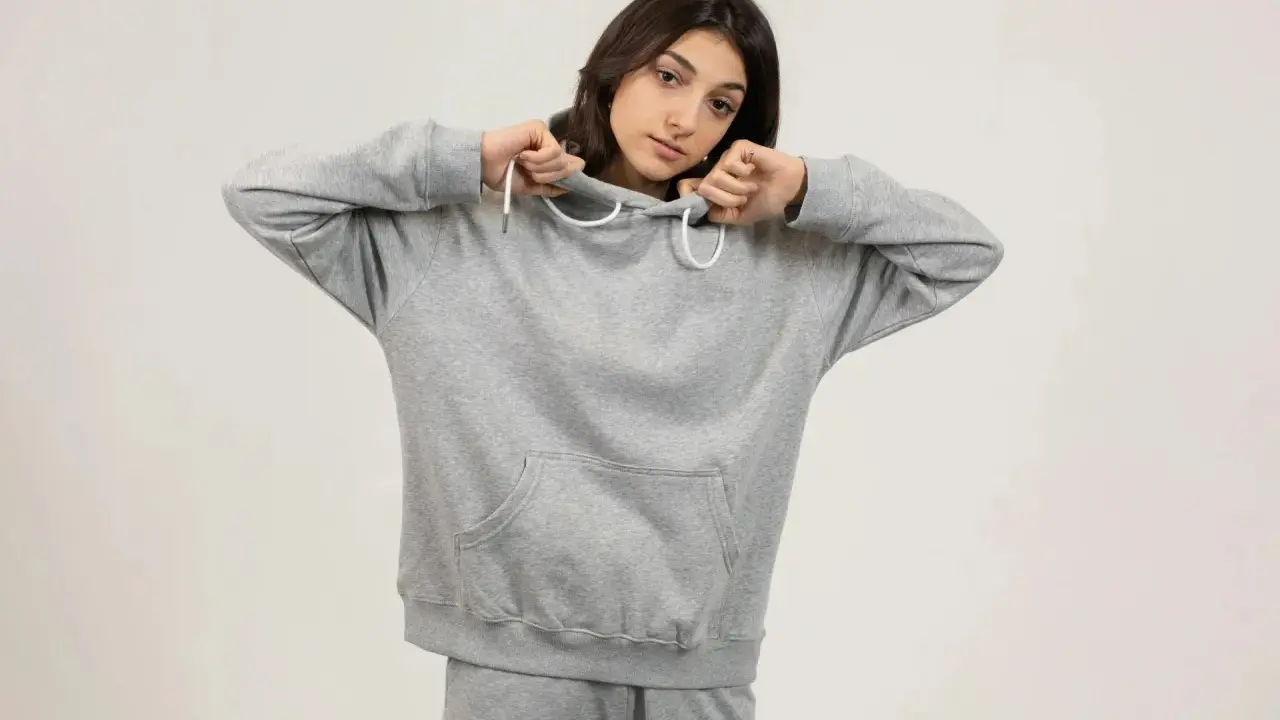 Dziewczyna w szarej bluzie oversize, z kapturem naciągniętym na głowę, pokazuje, jak nosić ten wygodny element garderoby.