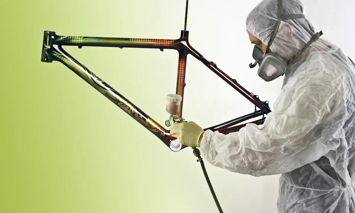 Person in Schutzanzug lackiert kunstvoll einen Rennrad Rahmen mit Spraydose.
