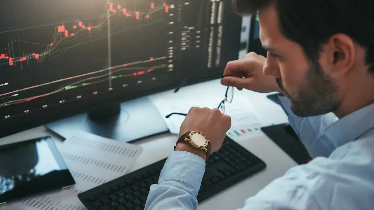 Un trader regarde sa montre, un chronophage qui le rappelle à l'ordre face aux graphiques boursiers.
