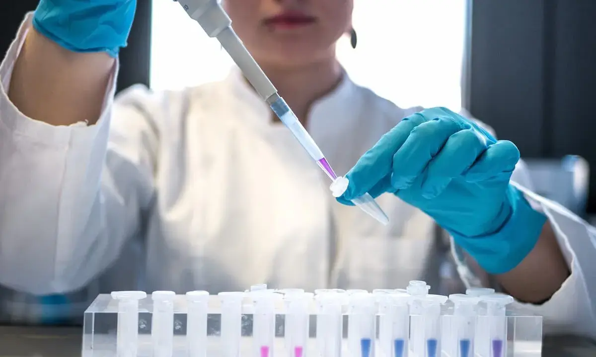 Naukowczyni w niebieskich rękawiczkach precyzyjnie pipetuje fioletowy płyn do probówki. To kluczowy etap w badaniach nad leczeniem biologicznym.