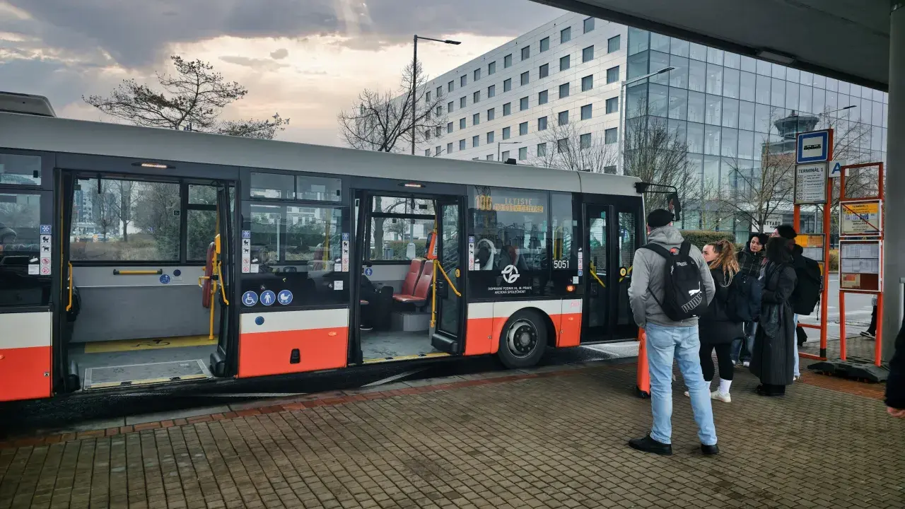 Buss vid flygplatsen, redo att ta resenärer från prag flygplats till centrum. En modern byggnad syns i bakgrunden.
