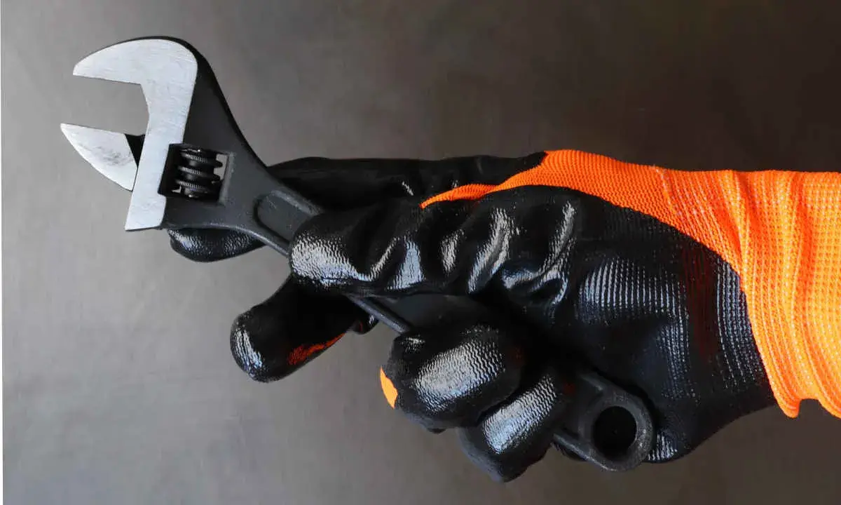 Mano enguantada sujeta llave inglesa ajustable, herramienta esencial para saber para que sirve la llave inglesa al apretar o aflojar tuercas y tornillos.