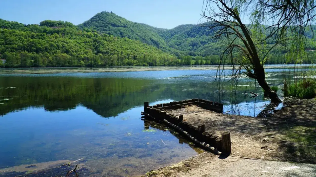 Un pontile in legno sul lago di Fimon, circondato da colline verdi e alberi.