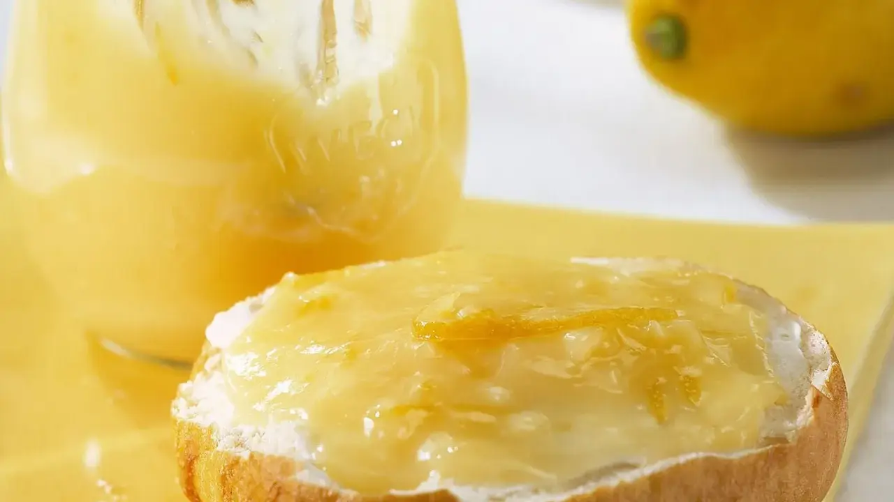Ein Brötchen mit cremigem Lemon Curd, das ist die Antwort auf die Frage: was ist Lemon Curd. Daneben ein Glas voller dieser gelben Köstlichkeit.