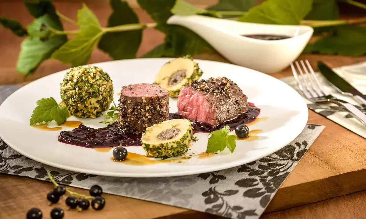 Edles Fleischgericht mit Johannisbeeren verwerten: zartes Rinderfilet, umhüllt von Kräutern und Nüssen, serviert mit einer fruchtigen Johannisbeersauce und Beilagen.