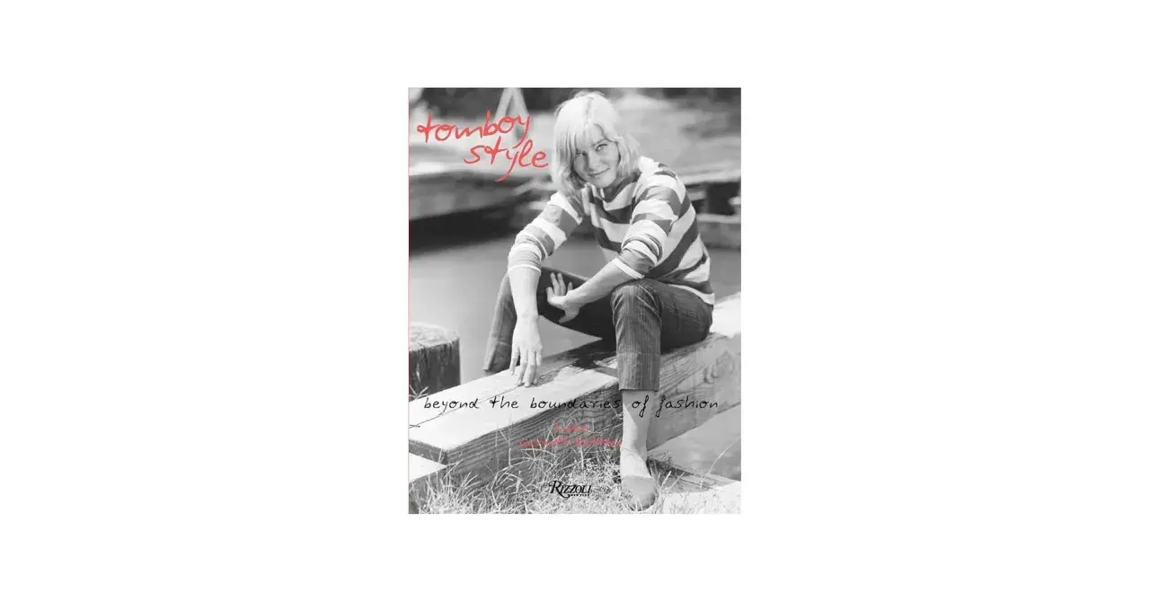 A woman with short blonde hair embodies tomboy style, wearing a striped shirt and jeans, sitting on a wooden beam. Text reads "tomboy style" and "beyond the boundaries of fashion.