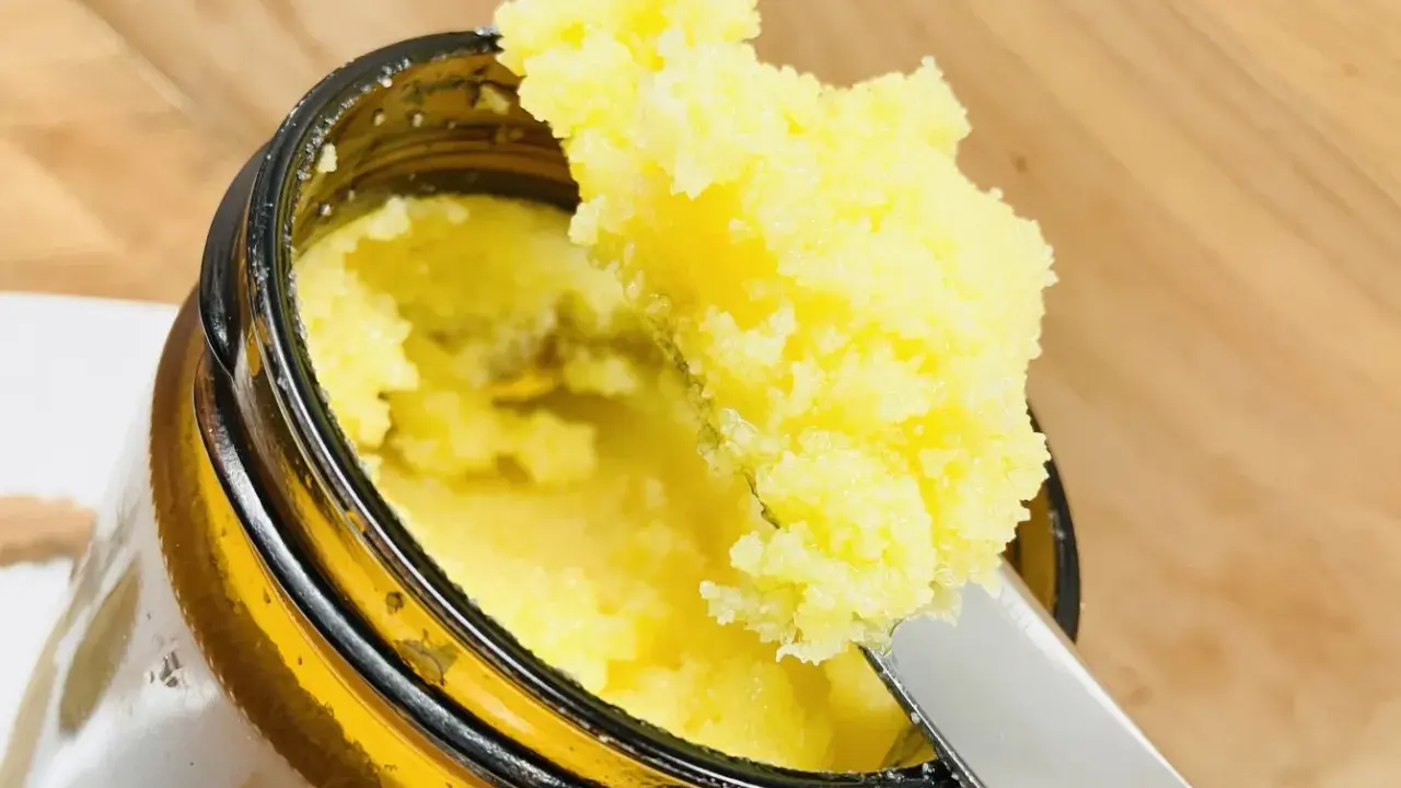 Ein Löffel entnimmt goldgelbes Ghee aus einem Glas. Was ist Ghee? Ein geklärte Butter, ideal zum Kochen und Backen.