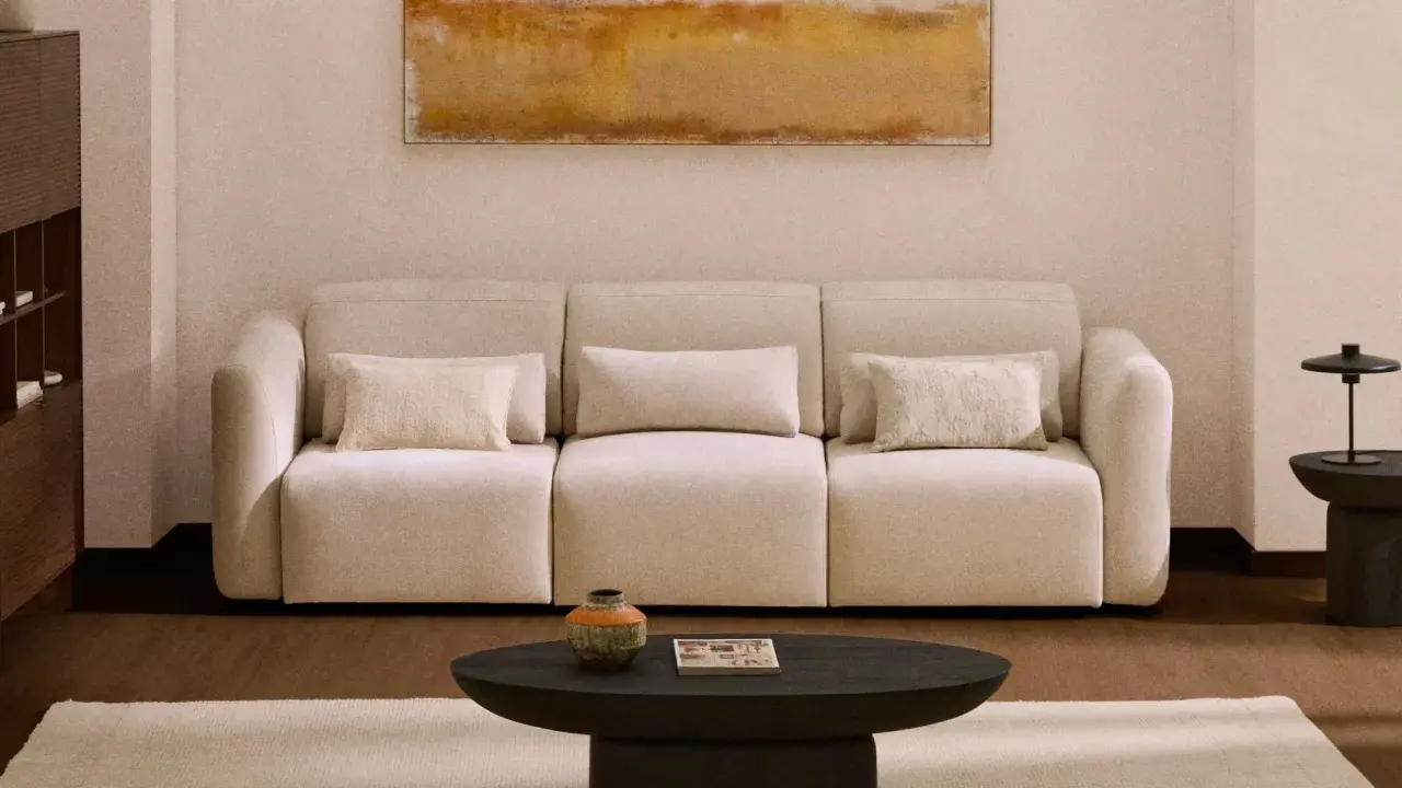 Sofá beige con cojines, mesa de centro oscura, alfombra clara y cuadro abstracto. Los colores feng shui crean un ambiente sereno.
