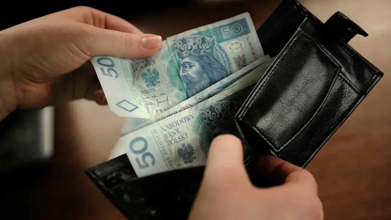 Ręce wkładają polskie banknoty 50 zł do czarnego portfela. To kieszonkowe dla dziecka na drobne wydatki.