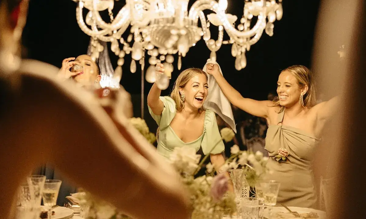 Mujeres brindando y riendo bajo una lámpara de araña. ¡Salud! Frases de brindis para celebrar la alegría.