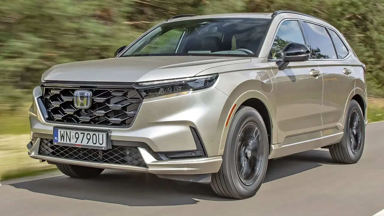 Nowy Honda CR-V w kolorze złotym jedzie po drodze, otoczony zielenią.
