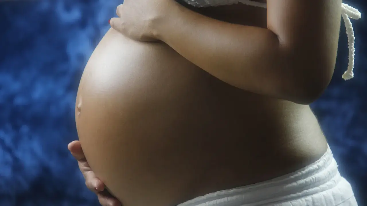 Pancia di donna incinta, con mani che la accarezzano. Si intravede un bikini bianco e uno sfondo blu. L'addome è tonico, forse con un leggero intestino iperecogeno visibile.