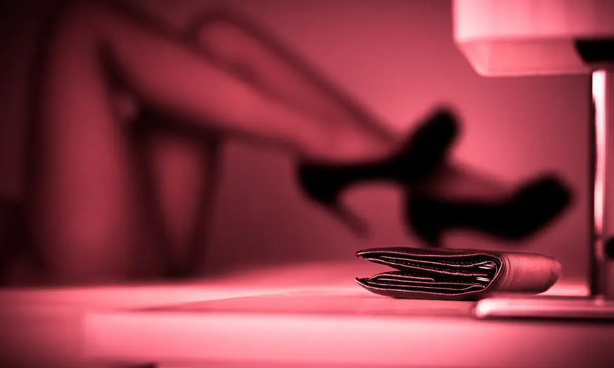 Portfel na stole, w tle niewyraźne nogi w szpilkach. To może być symbol tego, czym jest sexworking.
