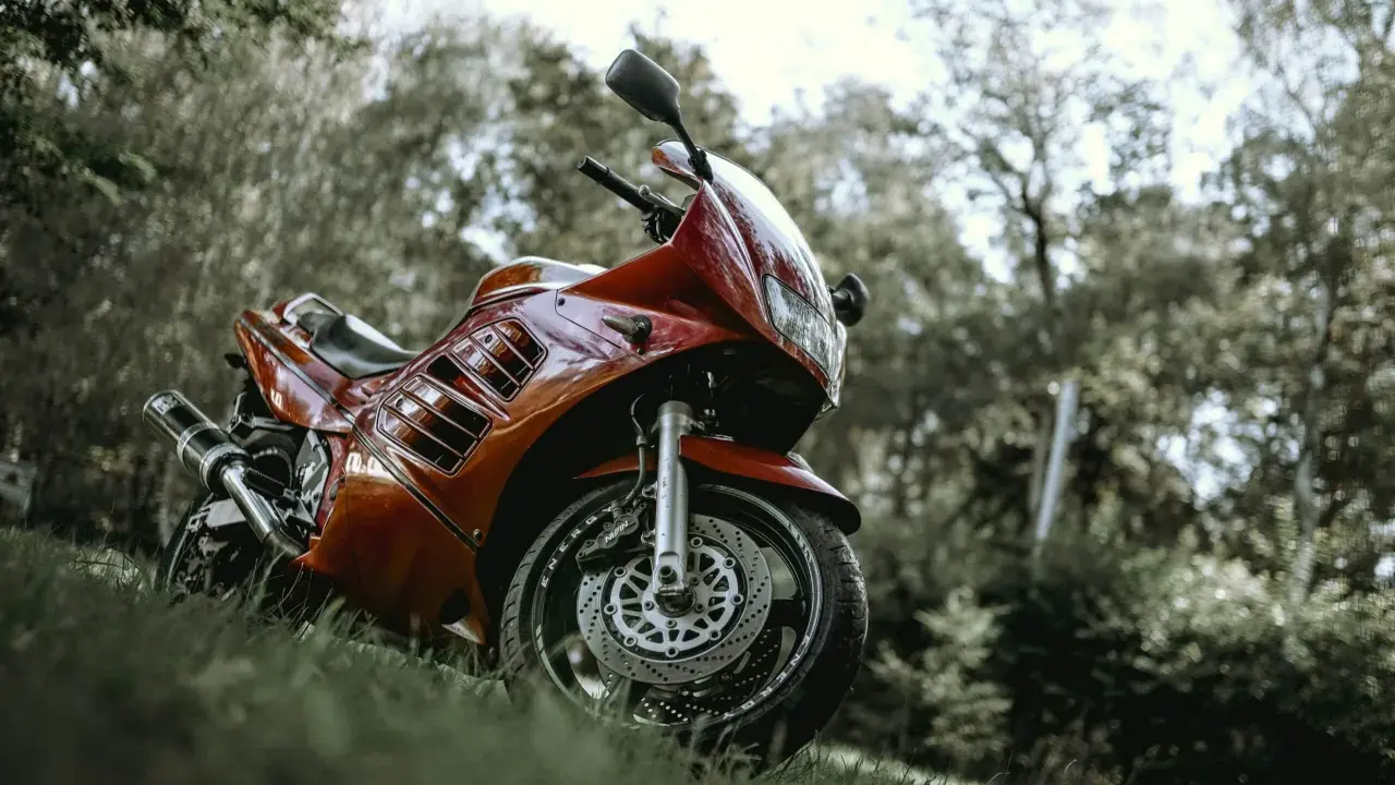 Czerwony motocykl Suzuki RF 900, zaparkowany na trawie wśród drzew. Idealny do sprawdzenia jego danych technicznych.