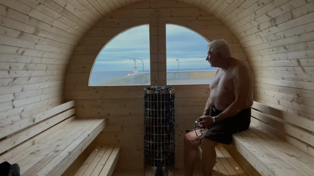 Man njuter av värmen i en bastuflotte i Skåne med utsikt över havet och en fyr.