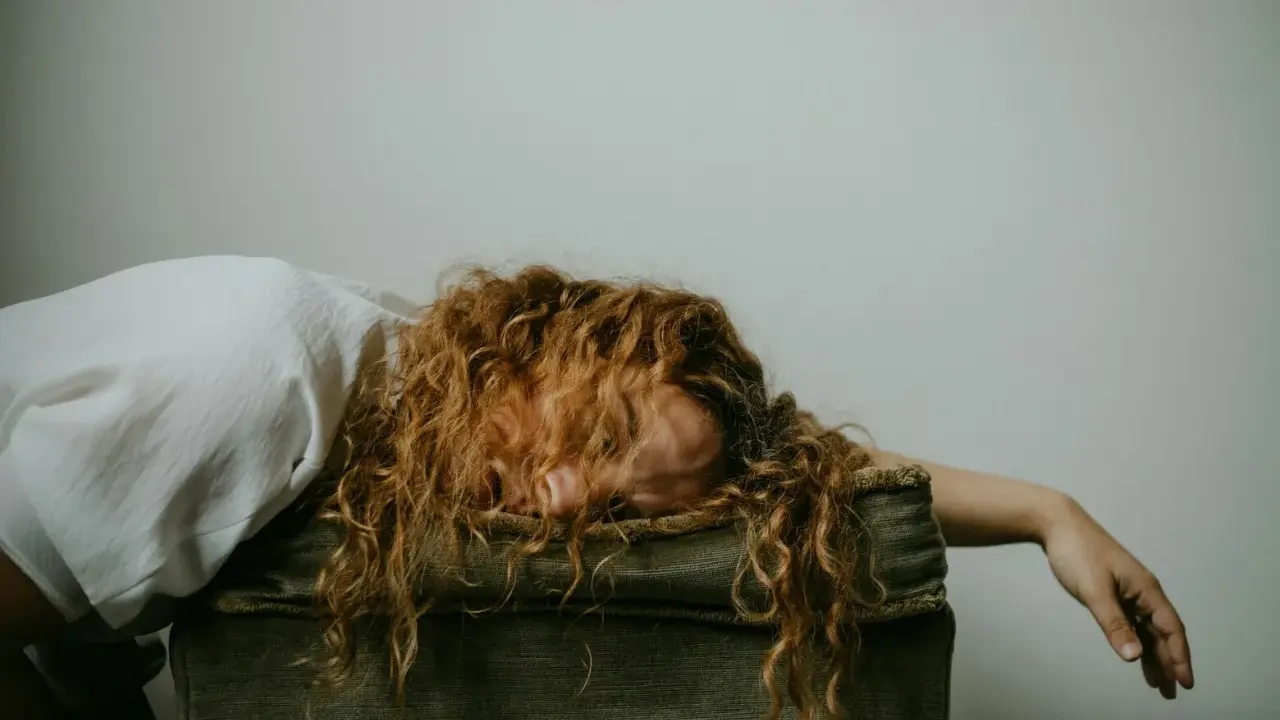 Donna con capelli rossi ricci, viso nascosto, sembra sopraffatta, forse un attacco di panico o uno svenimento.