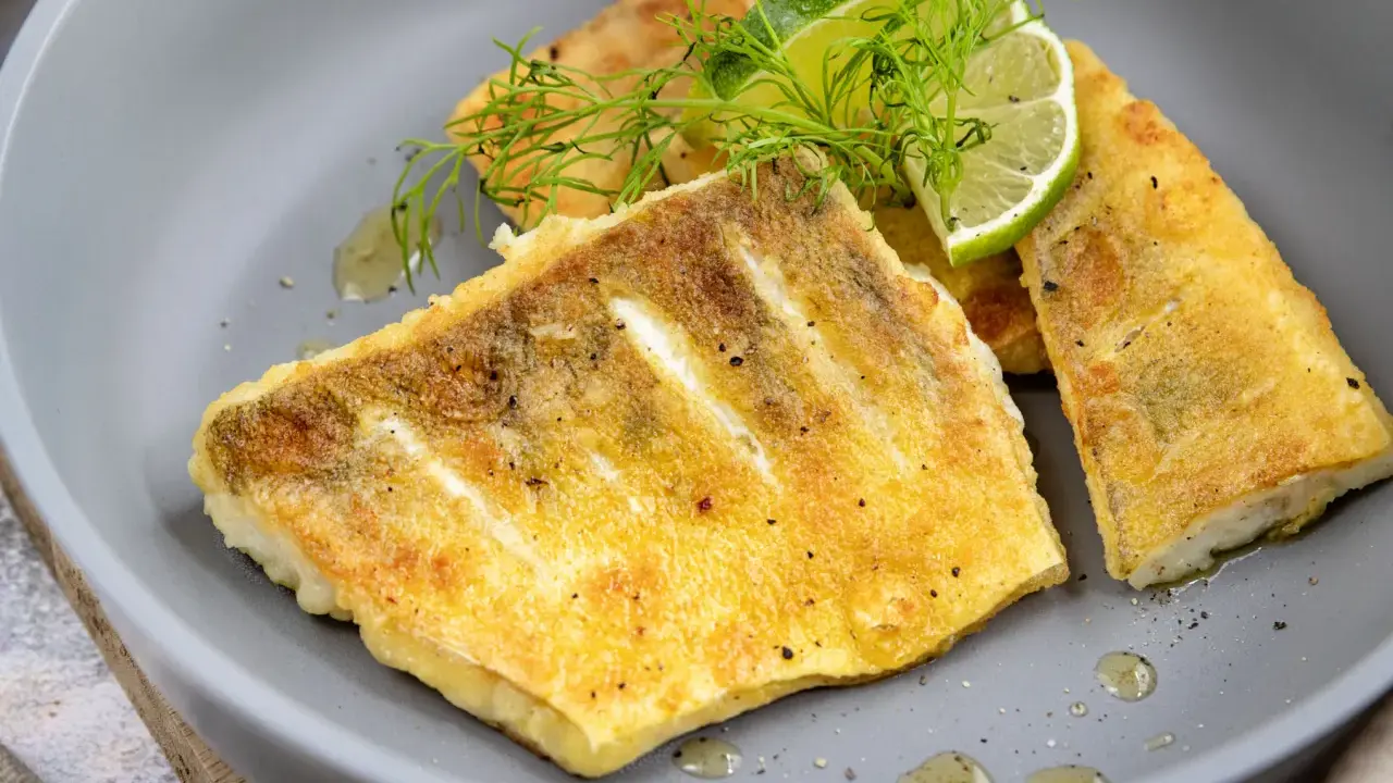 Zanderfilet ohne Haut braten: goldbraune Fischfilets auf grauem Teller, garniert mit Dill und Limettenspalten.